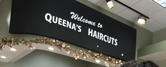 The black “Welcome to Queena's Haircuts” sign above the salon floor