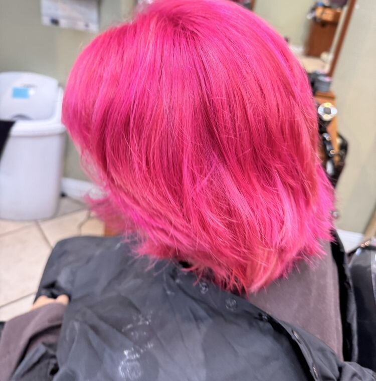 Layered shoulder-length hair colored bright pink, seen from behind in the salon chair